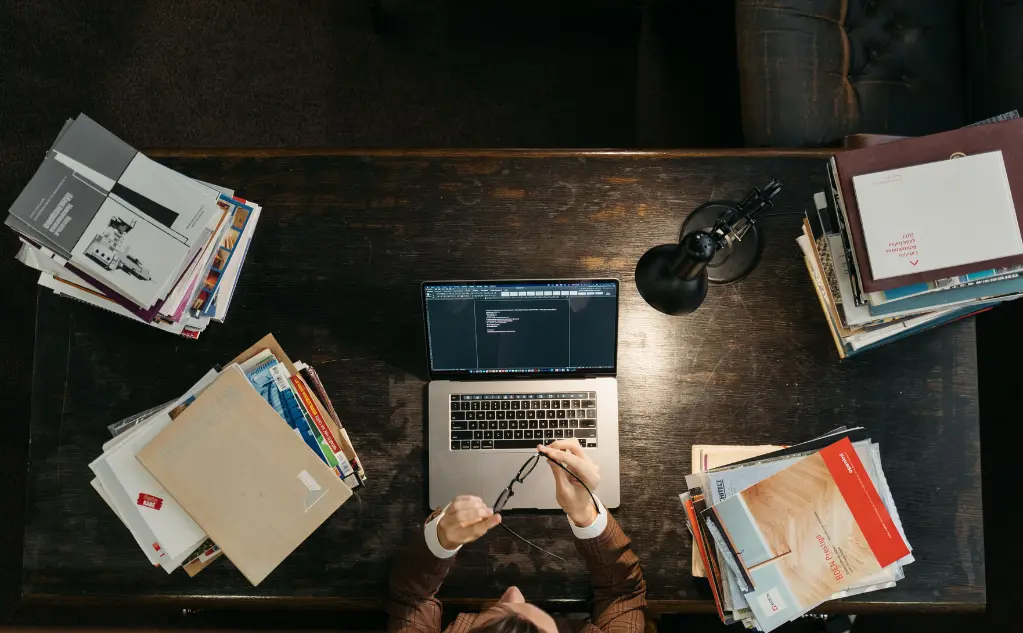 Person working at a desk surrounded by stacks of books and papers
